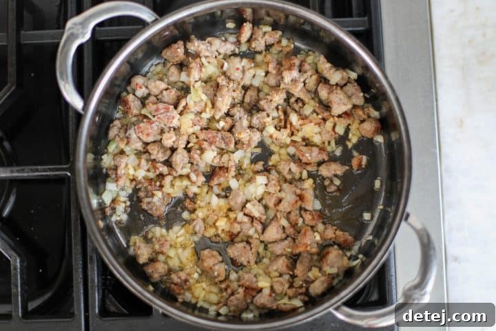 Ground Italian sausage browning in a hot pan, broken into smaller pieces with a spatula.