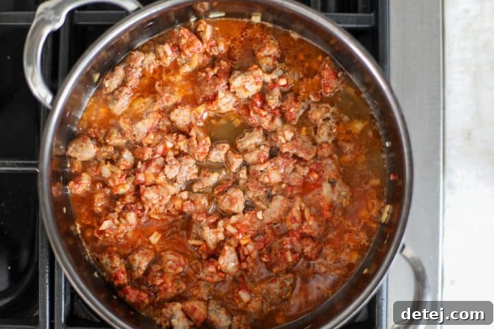 The sausage, aromatics, and caramelized tomato paste being deglazed with chicken broth, scraping up the fond from the pan.