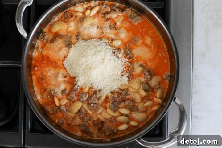 Grated Parmesan cheese being added to the creamy butter bean and sausage mixture in the pan, ready to be stirred until melted.