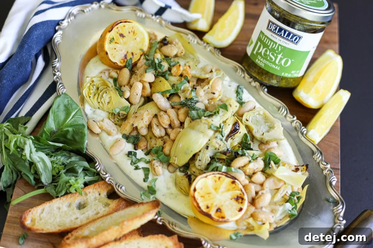 Roasted artichokes and beans with a jar of pesto alongside a serving dish.
