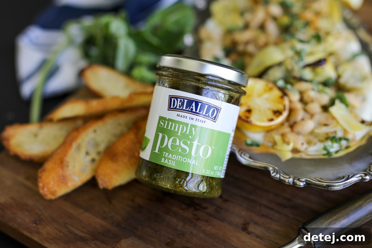 Jarred pesto leaning up against a dish of roasted artichokes and beans.