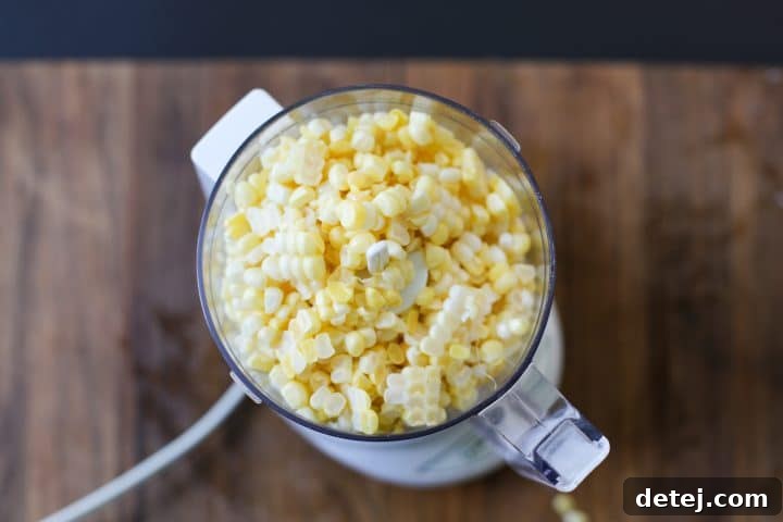 Fresh corn kernels being added to a food processor, ready to be blended for the corn puree.