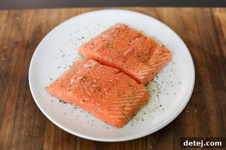 Two salmon fillets, seasoned with salt and pepper, lightly drizzled with oil, ready for grilling.