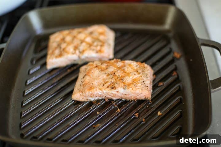 Two salmon fillets searing in a hot grill pan, showing grill marks and developing a crispy skin.