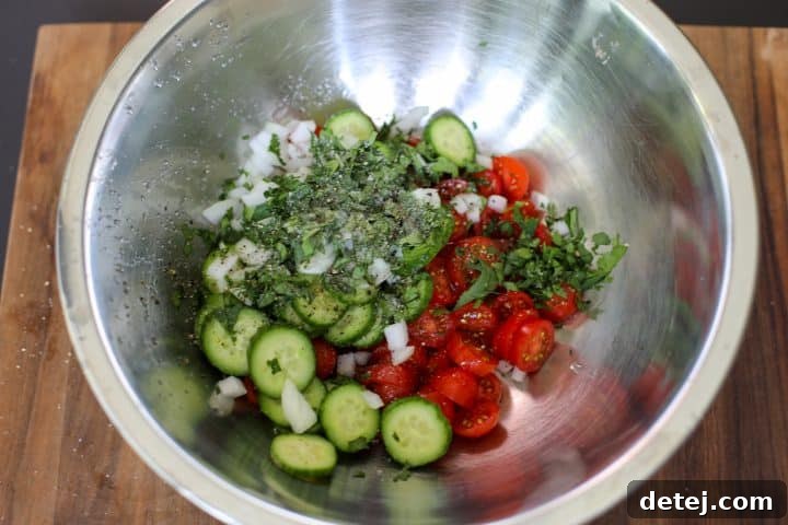 A vibrant tomato, cucumber, and herb salad in a bowl, dressed and ready to be served.