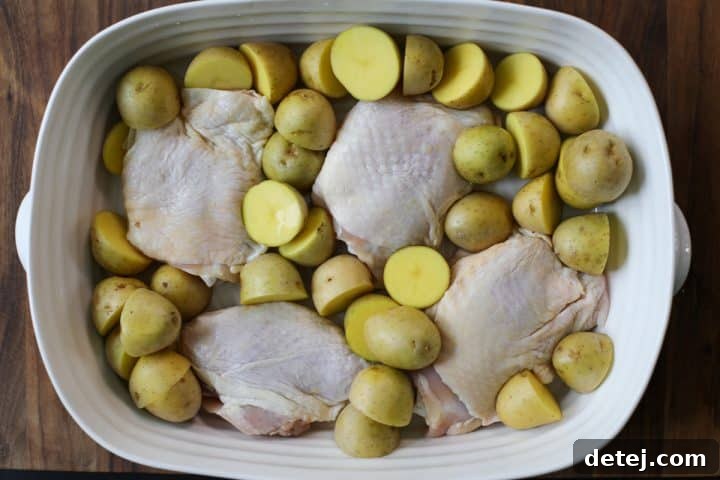 Raw chicken thighs and halved baby potatoes arranged in a baking dish, ready for seasoning.