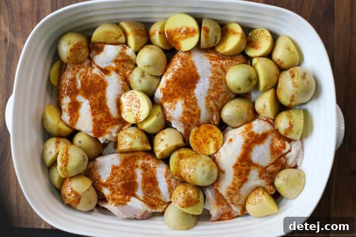 Avocado oil and lemon juice being drizzled over raw chicken and potatoes in a baking dish.