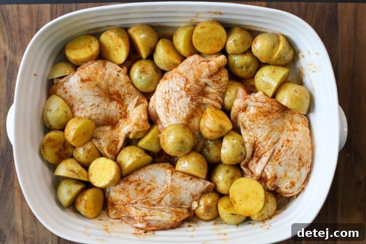 Raw chicken and potatoes fully coated in the homemade spice blend, ready for roasting.