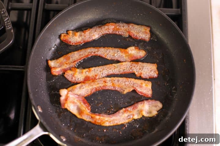 Ultimate Breakfast Chicken Cutlets 5 bacon in a pan, cooking to a perfect crispness for the chicken cutlets.