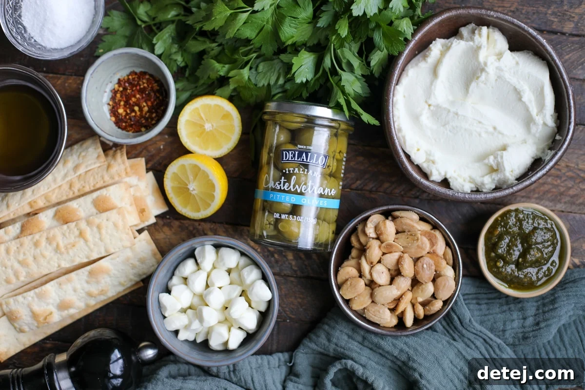 Various ingredients laid out for the olive and cheese dip recipe, including olives, mozzarella, fresh herbs, and a jar of pesto.