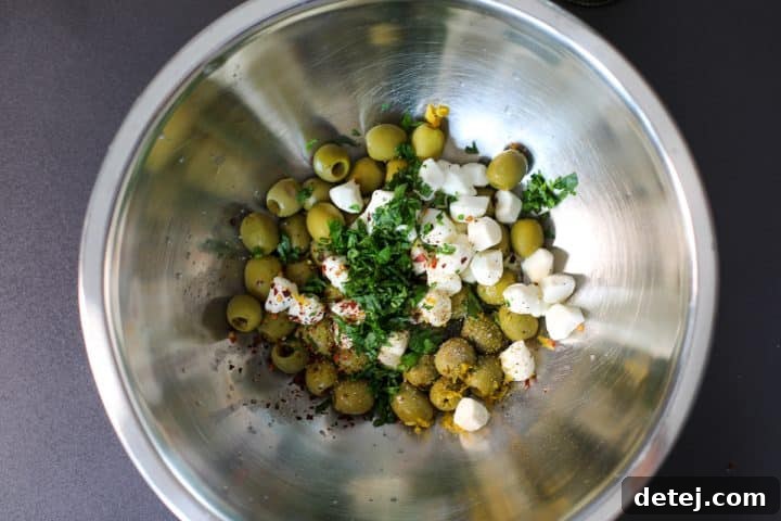 A bowl of olives, mozzarella, and herbs being mixed together for the marinade.