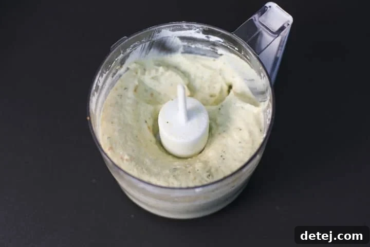 Ricotta cheese, pesto, and Greek yogurt being blended in a food processor to create a smooth, whipped mixture.