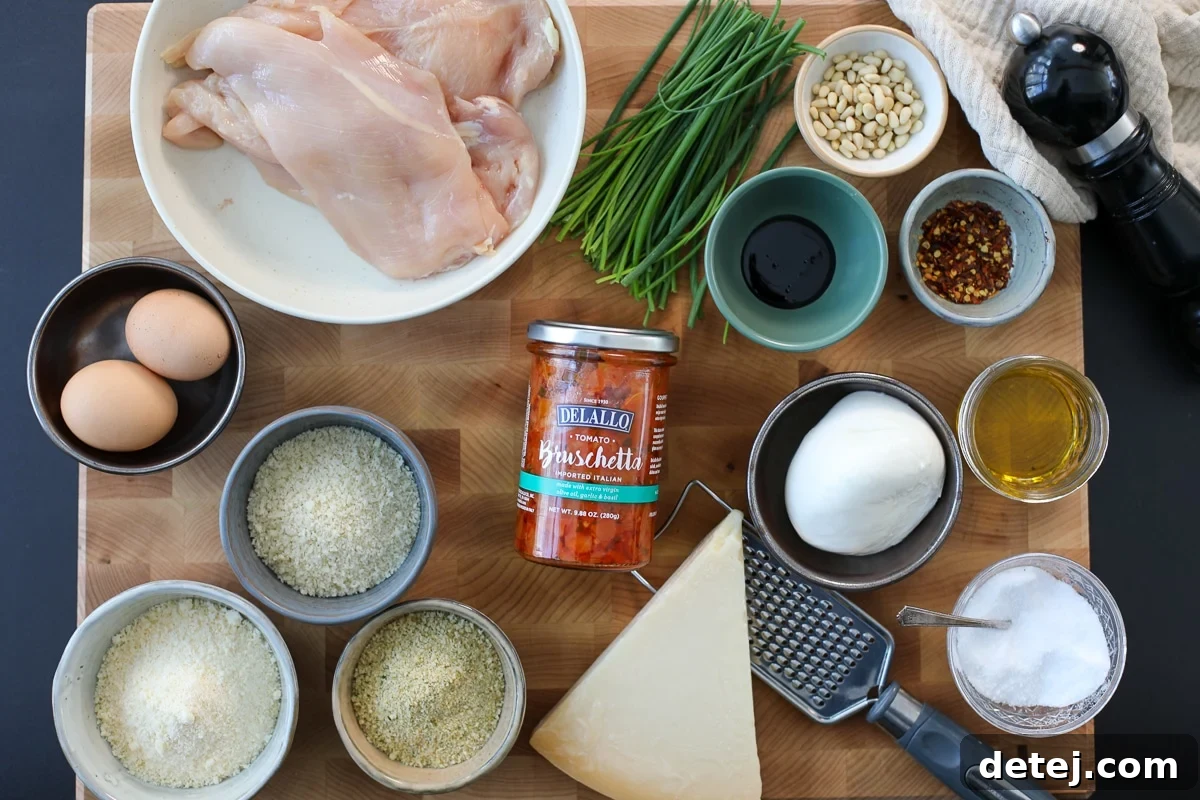 A selection of fresh ingredients including burrata cheese, Delallo bruschetta, pine nuts, and chicken breasts, laid out for the recipe.