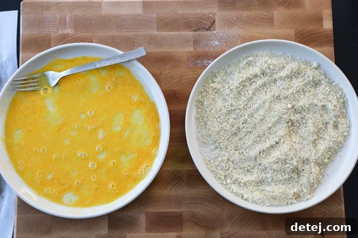 Three plates set up for breading chicken cutlets: one with whisked eggs, one with a breadcrumb mixture, and one empty plate for finished cutlets.