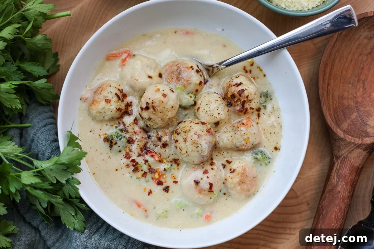 A bowl of healthy broccoli cheddar soup with mini chicken meatballs, garnished with fresh herbs.