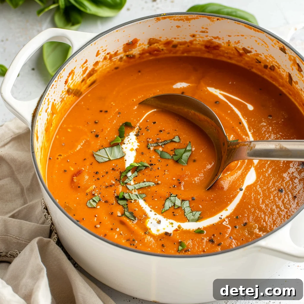A steaming bowl of creamy tomato soup garnished with fresh basil leaves.