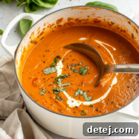 A close-up shot of creamy tomato soup with a swirl of cream and fresh herbs.