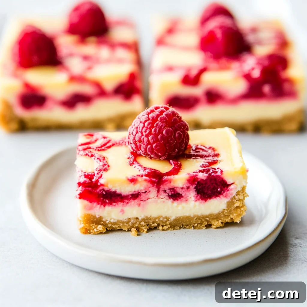 Close-up of a perfectly sliced Raspberry Lemon Cheesecake Bar, garnished with fresh raspberries and a light dusting of powdered sugar, presented on a white plate.