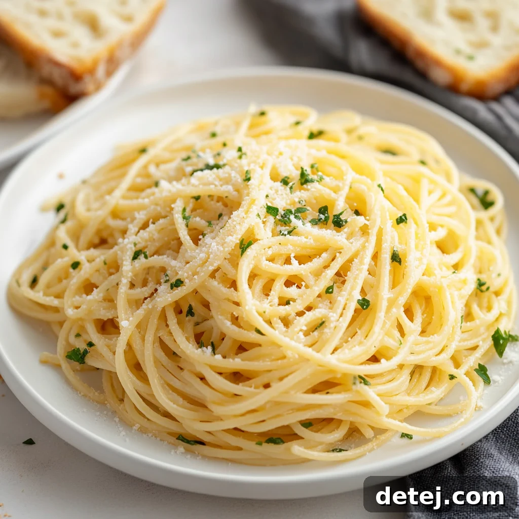 A top-down view of garlic butter noodles served in a white bowl, garnished with fresh parsley and a fork resting beside it.