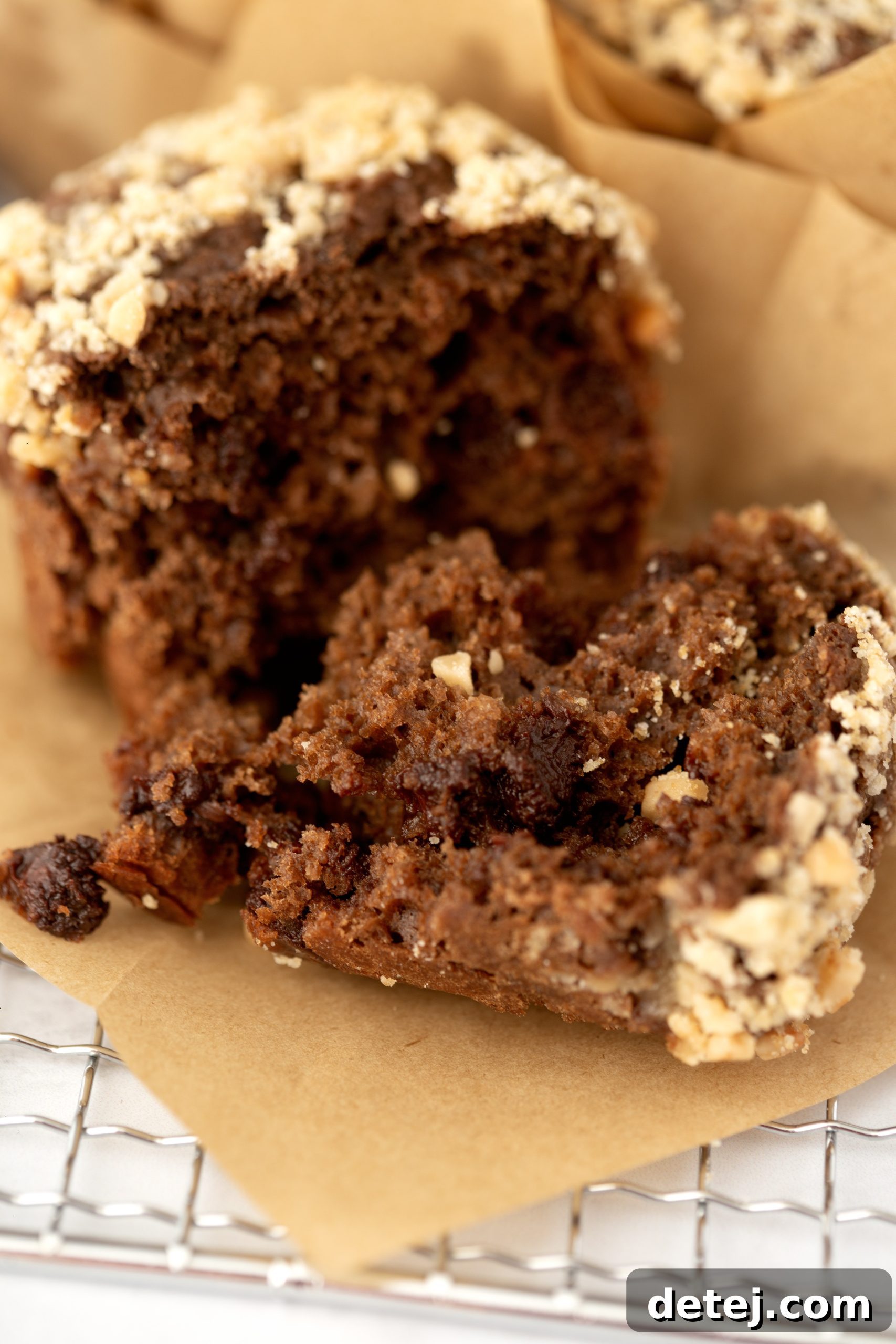 Freshly baked chocolate muffins with toffee crumble, one broken open to reveal the moist interior and melted chocolate chips.
