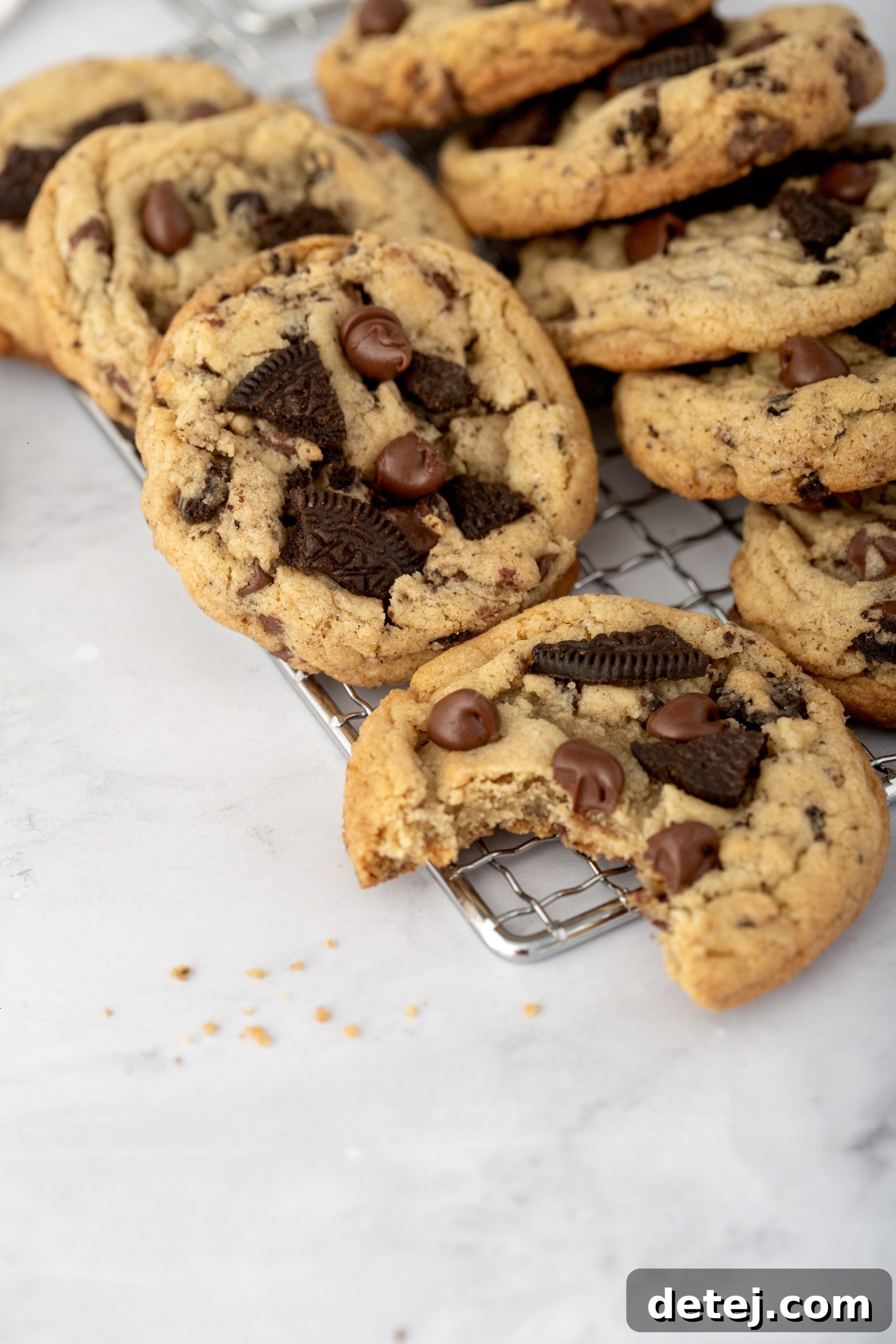 Hand reaching for a freshly baked bakery-style Oreo Chocolate Chip Cookie, with a background of more cookies.