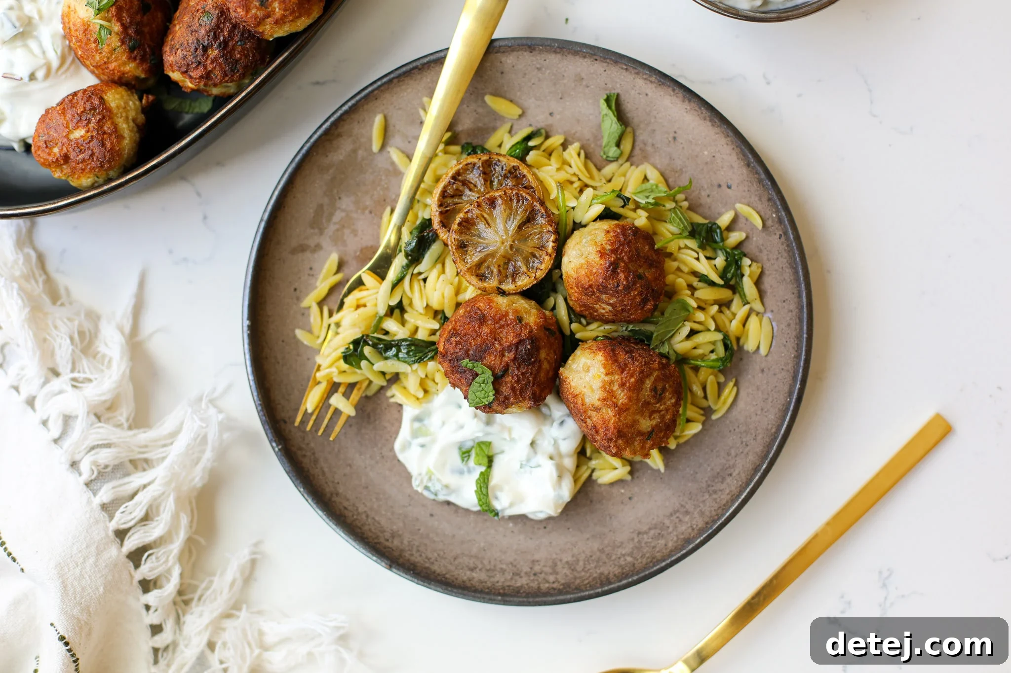 Beautifully plated Greek Chicken Meatballs with lemon butter orzo, tzatziki, and fresh herbs.