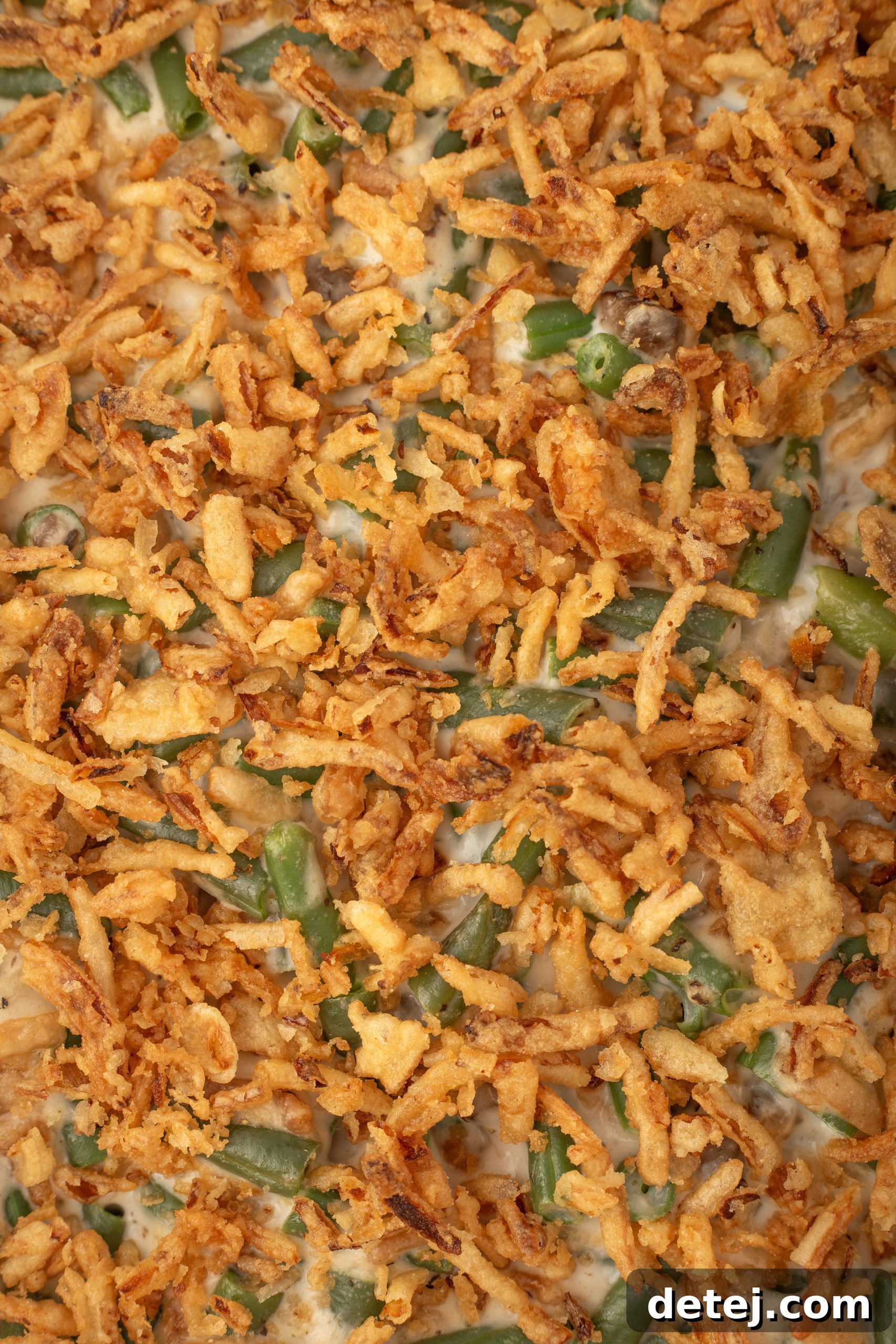 Hands sprinkling French fried onions over a partially baked green bean casserole.