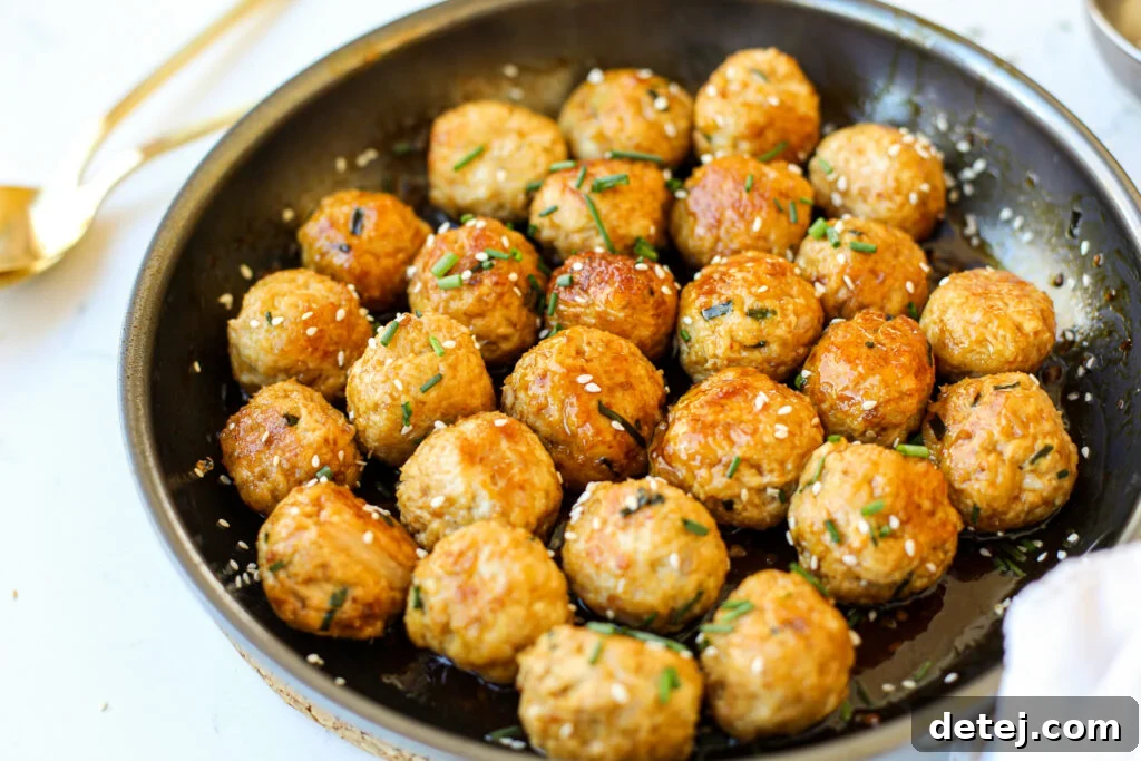 Sticky & Saucy Asian Meatballs 2 Plate of saucy Asian chicken meatballs garnished with sesame seeds and chives, ready to serve.
