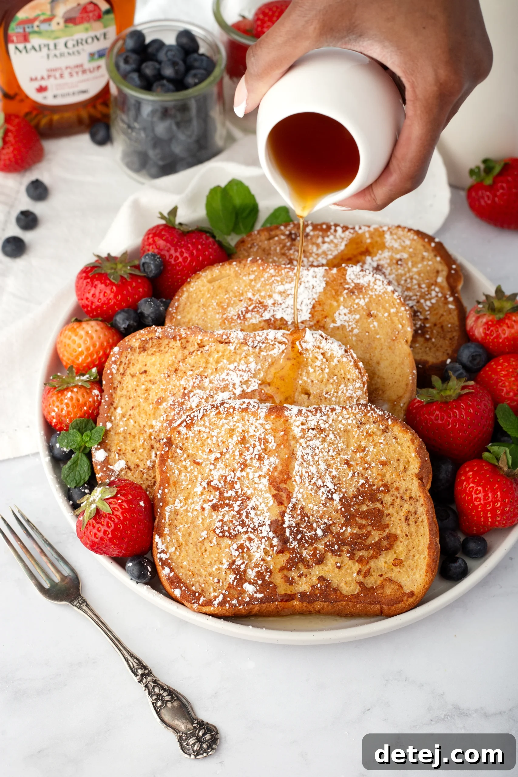 Golden brown French Toast slices on a plate with berries and syrup.