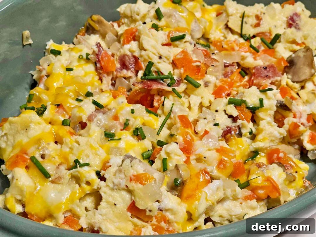 A vibrant plate of loaded scrambled eggs, garnished with chives and a side of crispy bacon.