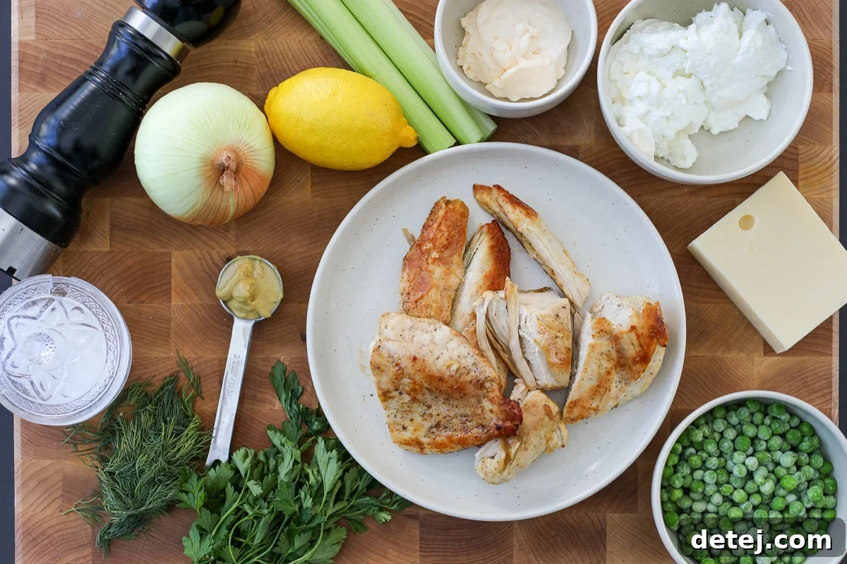 A collection of fresh, colorful ingredients laid out, including shredded chicken, vibrant peas, diced Swiss cheese, and herbs, all ready for the creamy chicken salad.