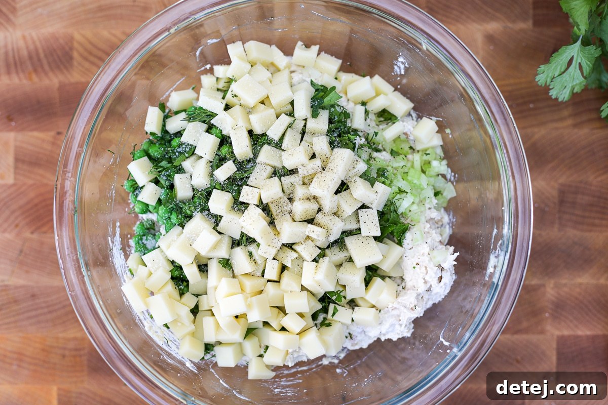 All salad ingredients, including peas, Swiss cheese, and herbs, mixed in a large bowl.