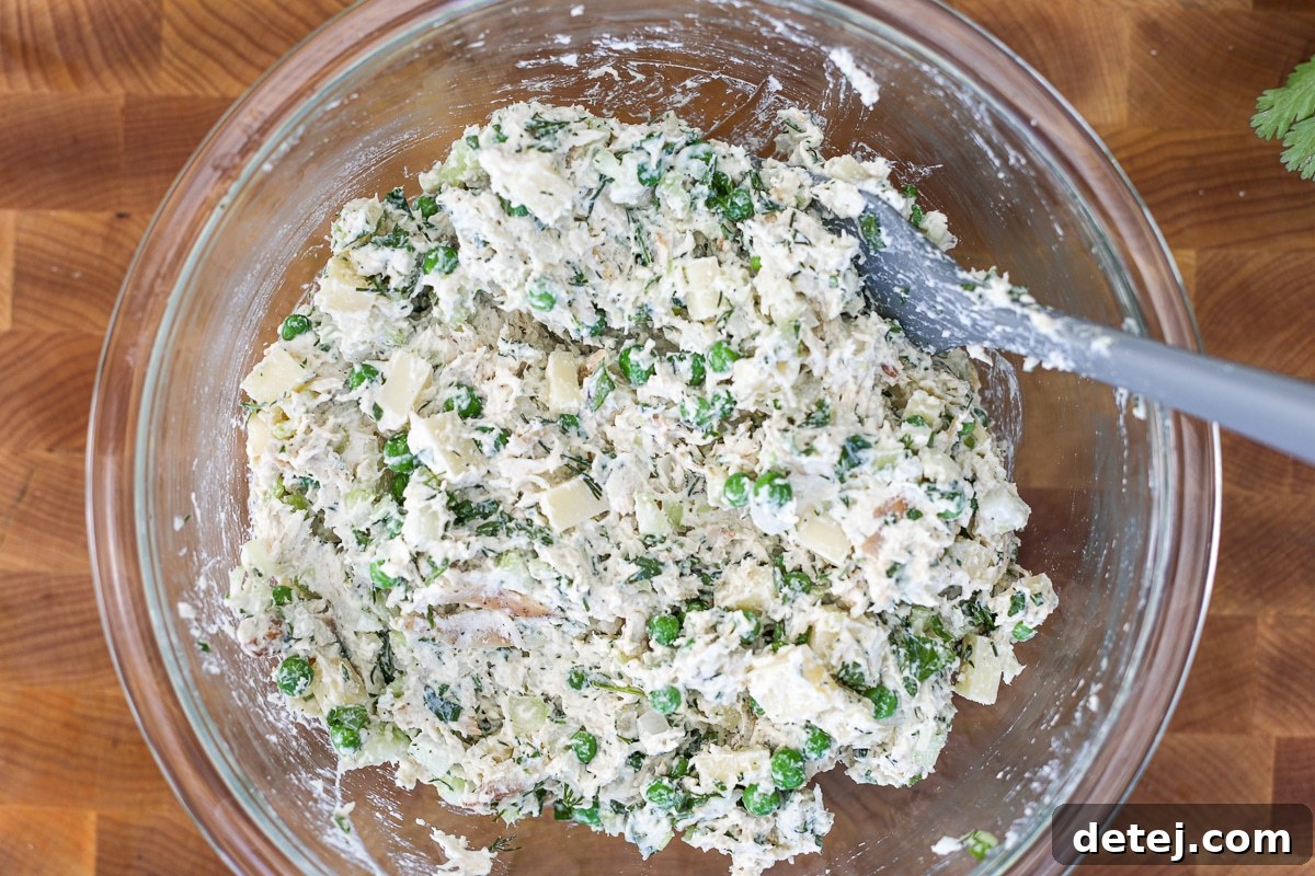 A large bowl of thoroughly mixed creamy chicken salad, vibrant and ready to serve.