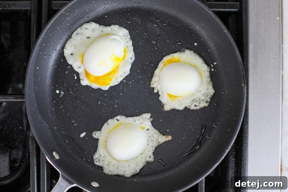 Egg halves placed onto melting cheese clusters in a nonstick pan, creating a crispy base.