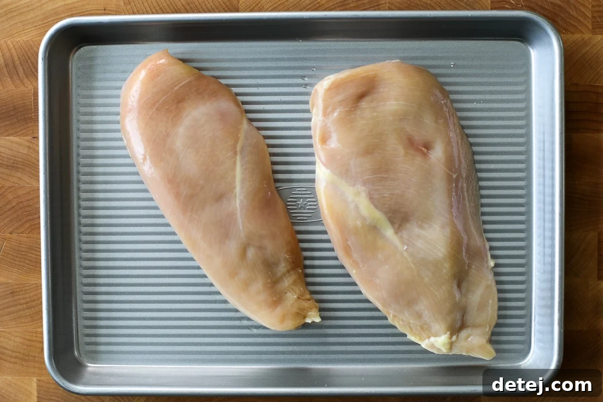 Chicken breasts seasoned on a baking tray before cooking.