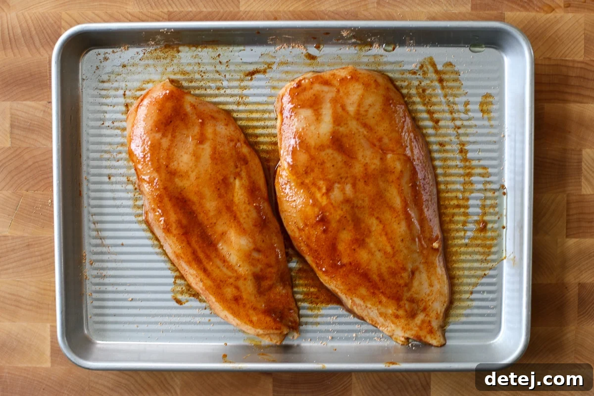 Another view of the chicken coated in seasoning on a baking tray.